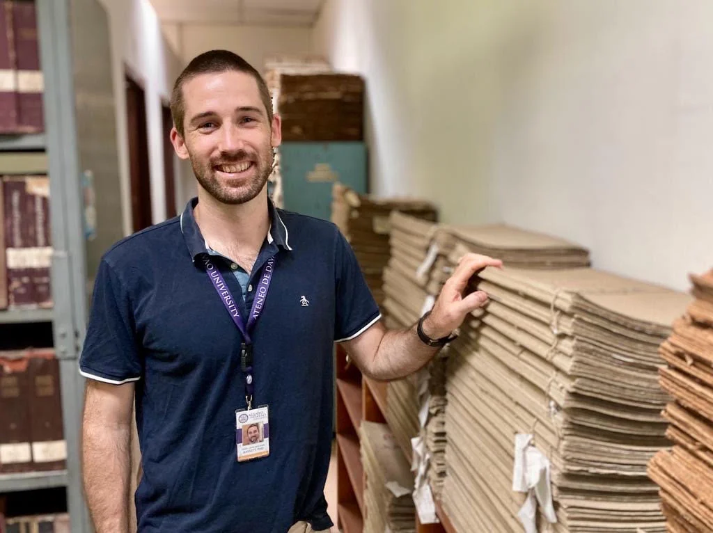 Johnny Bassett beside stacks of archival newspapers in Davao, Philippines